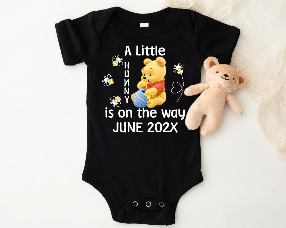 Baby onesie with Winnie the Pooh design and text 'A Little Hunny is on the way JUNE 202X' on a white background.