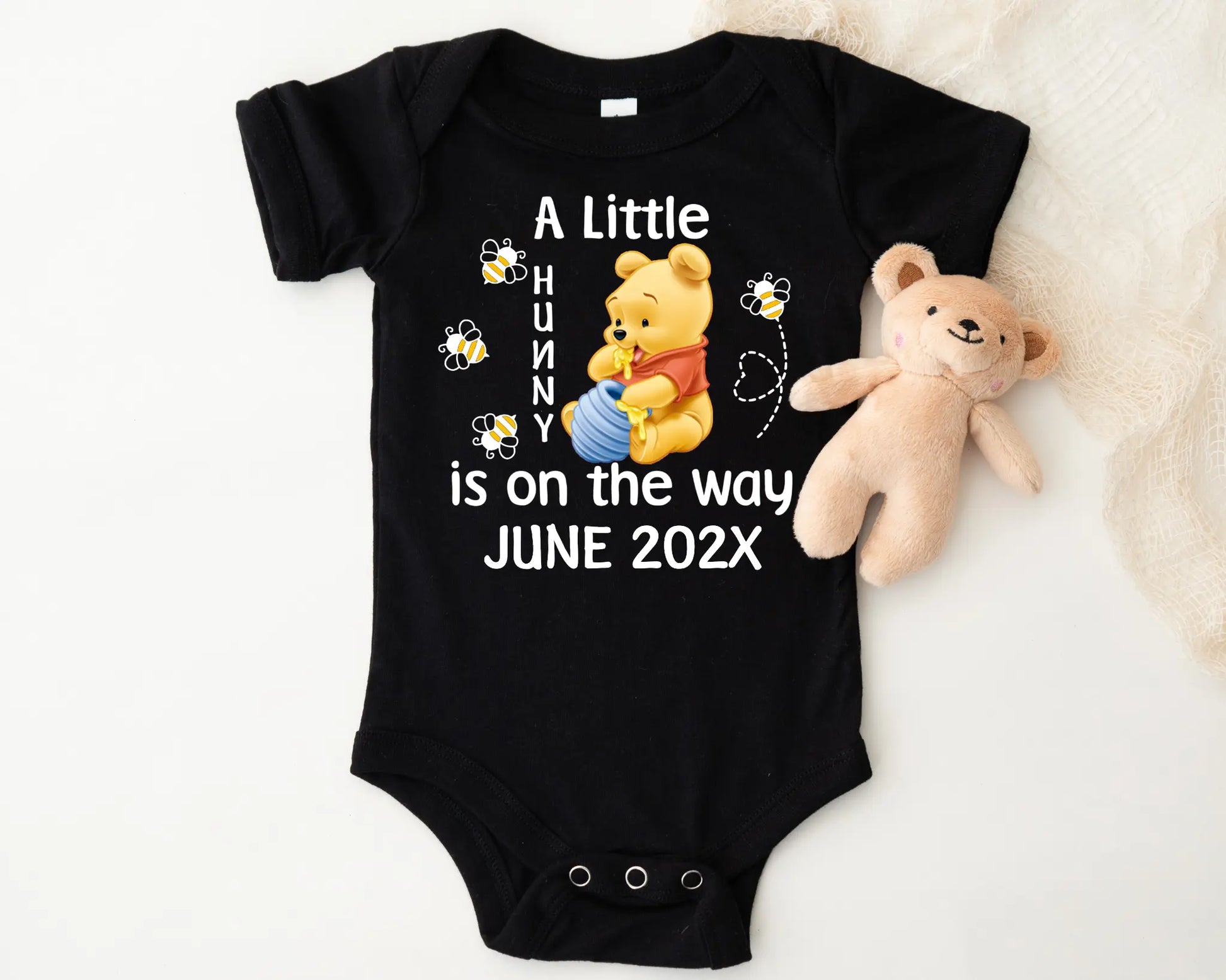Black baby onesie with Winnie the Pooh design and teddy bear on a white background