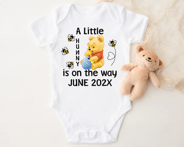 Baby onesie with Winnie the Pooh design and text 'A Little Hunny is on the way JUNE 202X' on a white background.