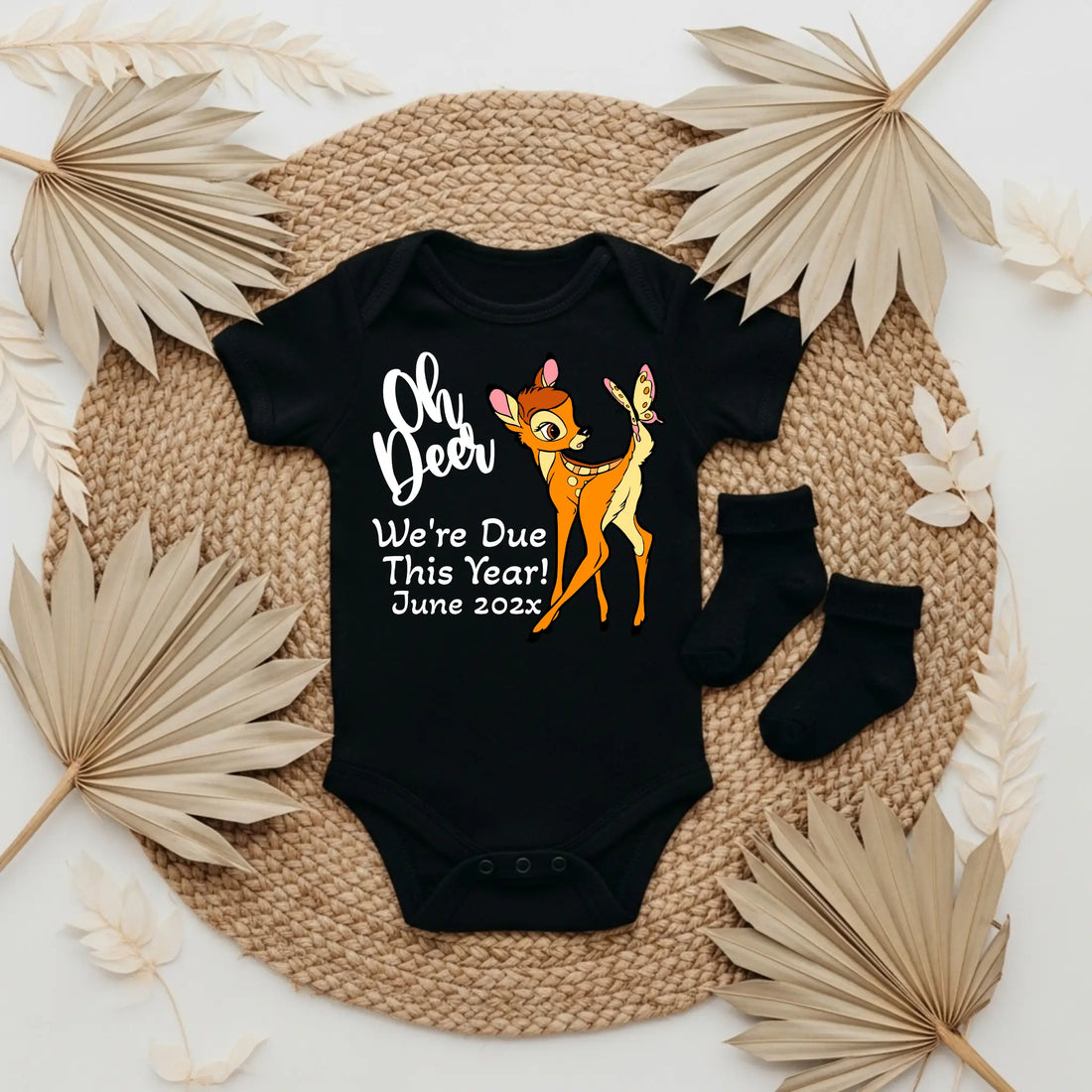 Baby onesie with 'Oh Deer We're Due This Year! June 202x' text and Bambi graphic on a textured surface.
