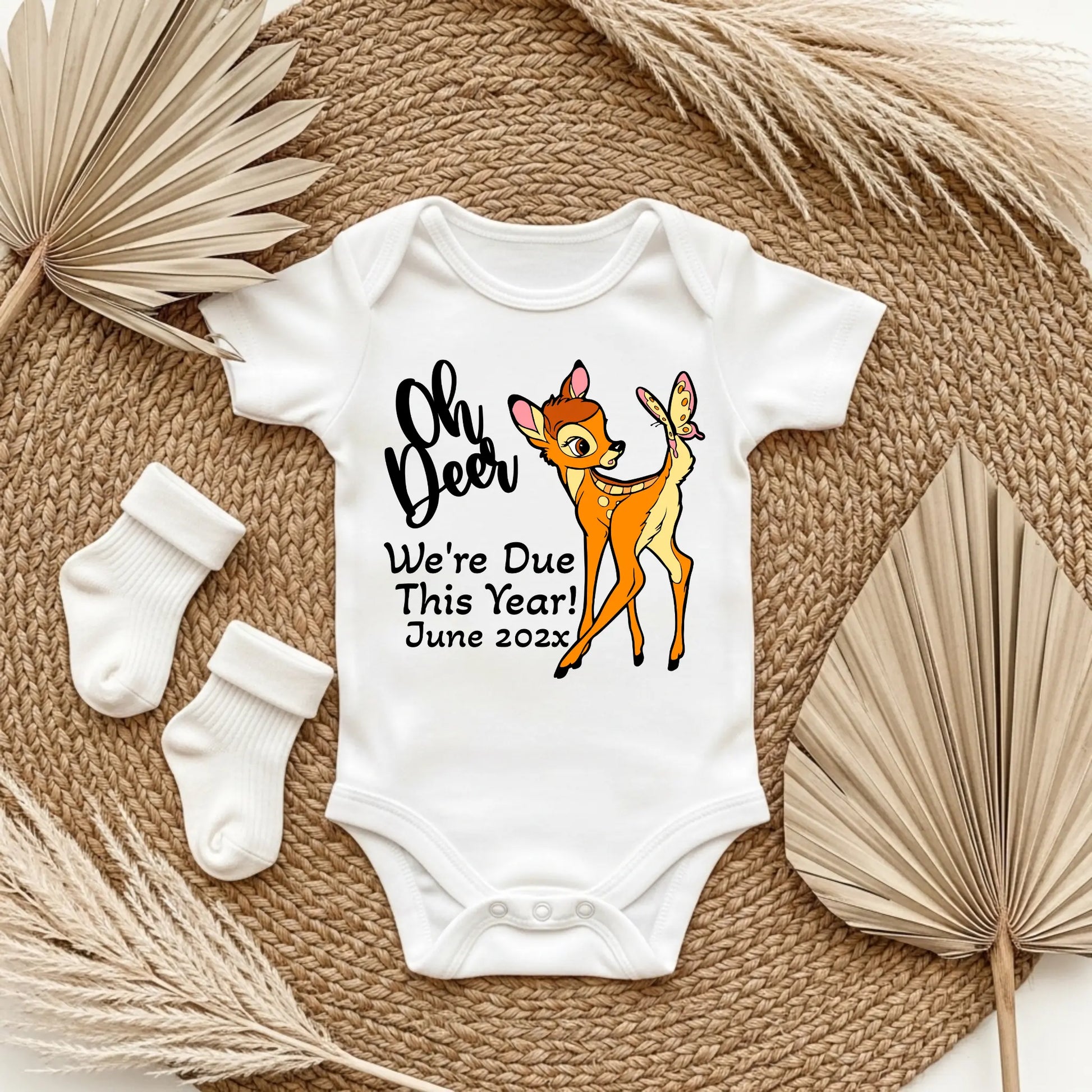 Baby onesie with 'Oh Deer We're Due This Year! June 202x' text and Bambi graphic on a textured surface.