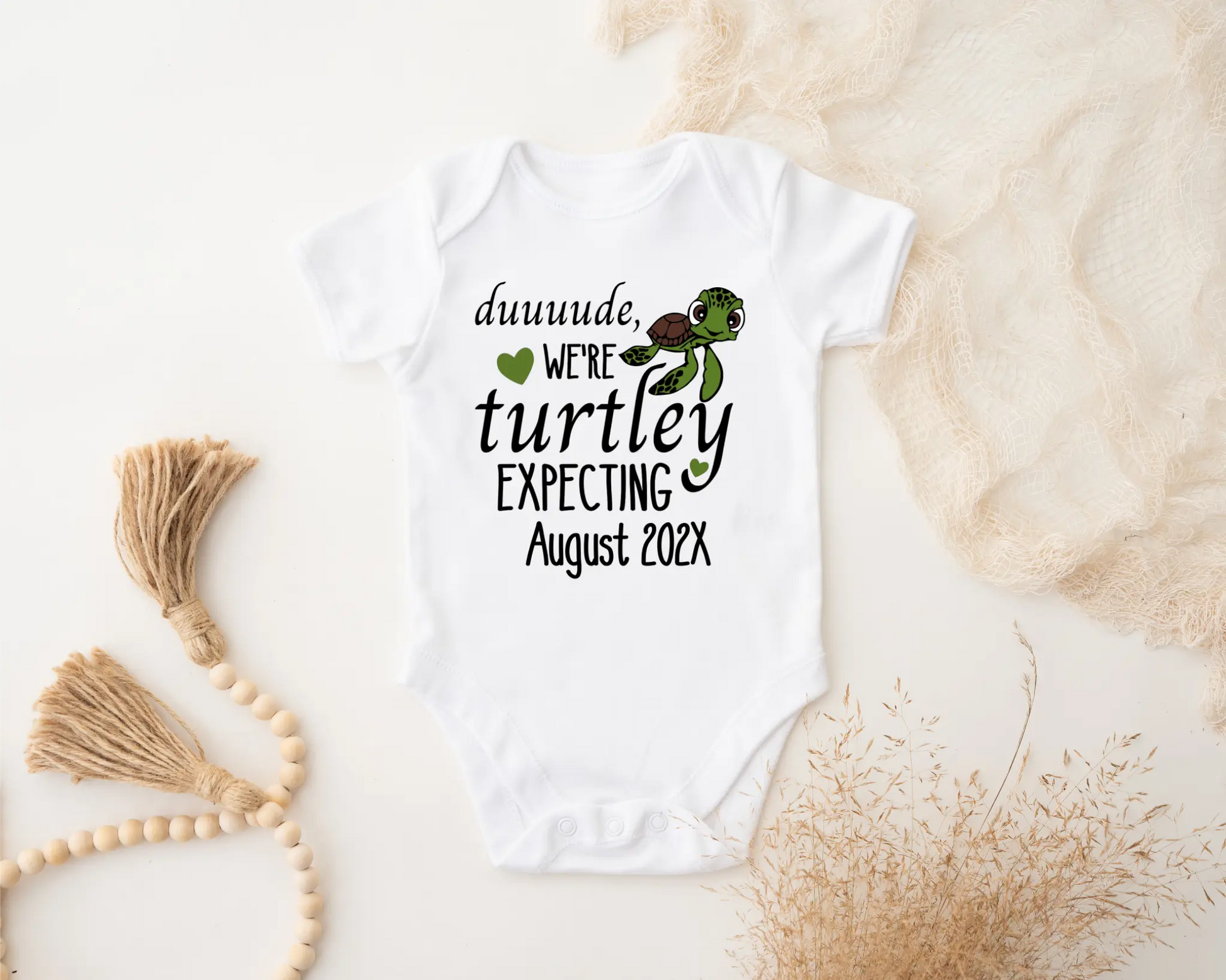 White baby onesie with turtle design and text on a textured beige surface.