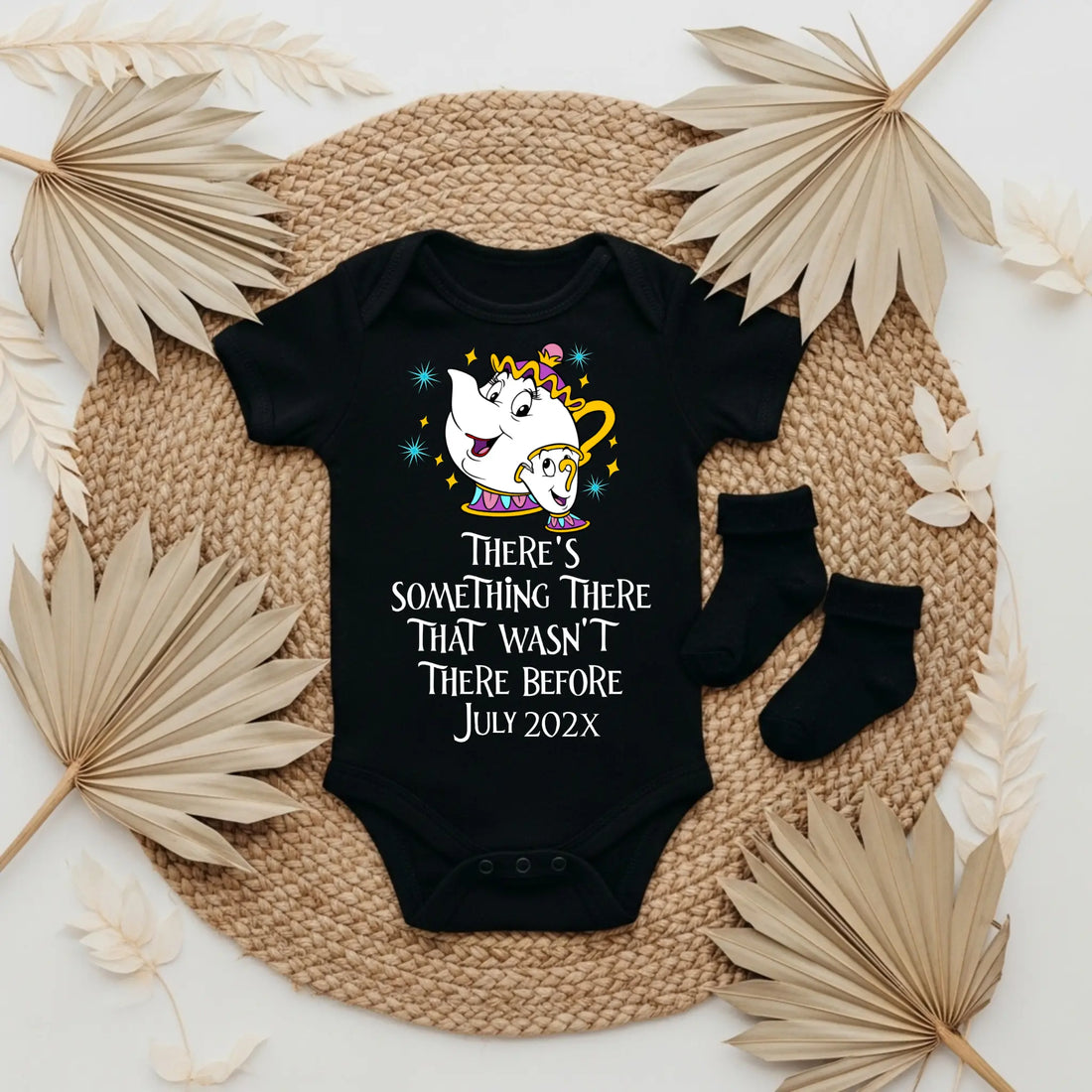 Baby onesie with a cartoon character and text, placed on a textured surface with socks and leaves.