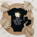 Black baby onesie with a cartoon design and text, placed on a woven mat with decorative leaves.