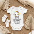 Baby onesie with a cartoon character and text, placed on a textured surface with socks and leaves.