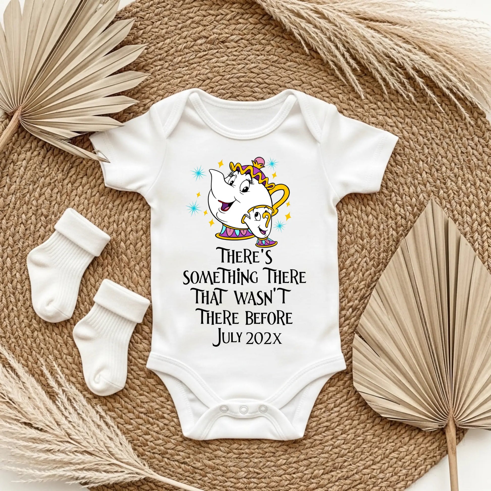 Baby onesie with a cartoon character and text, placed on a textured surface with socks and leaves.